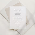Minimal wedding menu card featuring a centered serif layout with the title “Tastes of Love,” printed in soft black on off-white textured paper, styled with layered neutral envelopes in a clean, modern flat lay.
